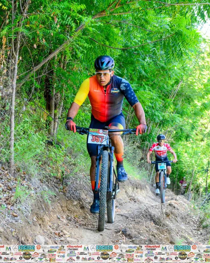 Ciclista en ruta de montaña en un sendero rodeado de árboles verdes, participando en una competencia.