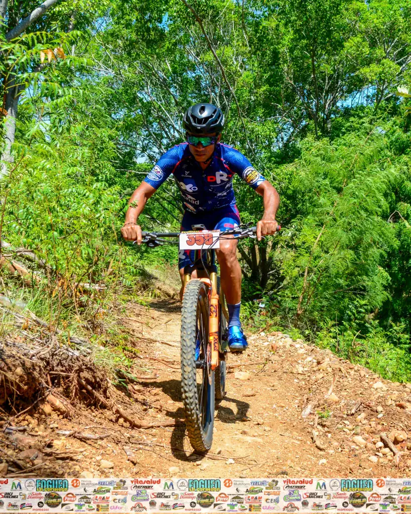 Ciclista en ruta de montaña en un entorno natural con árboles verdes y terreno rocoso.