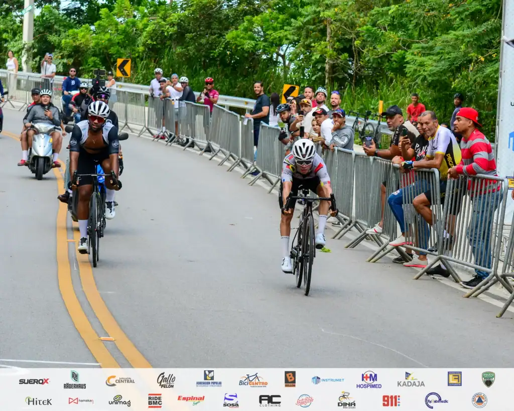 Ciclistas compitiendo en una carrera en la calle con espectadores y seguridad.