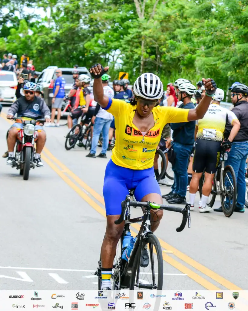 Ciclista con casco y uniforme amarillo en celebración tras ganar una carrera en la calle rodeado de.