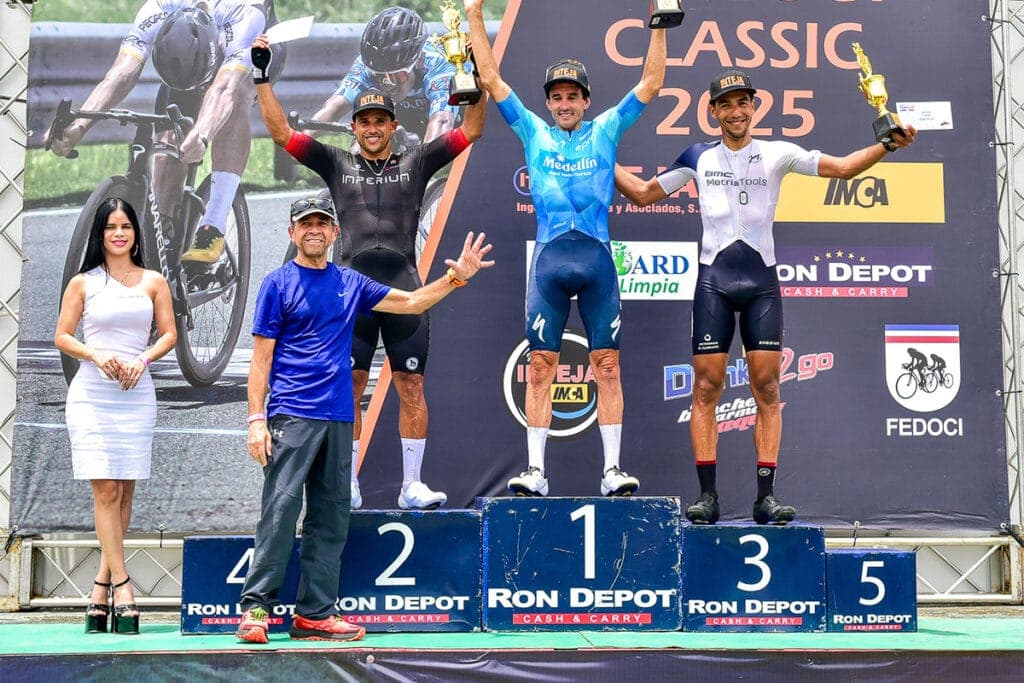Campeones en el podio de una carrera de ciclismo con trofeos y medallas.