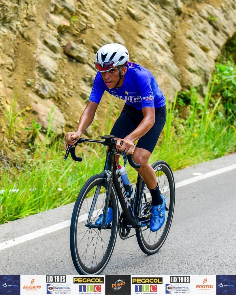 Ciclista en bicicleta de ruta en un camino de montaña con casco y ropa deportiva.